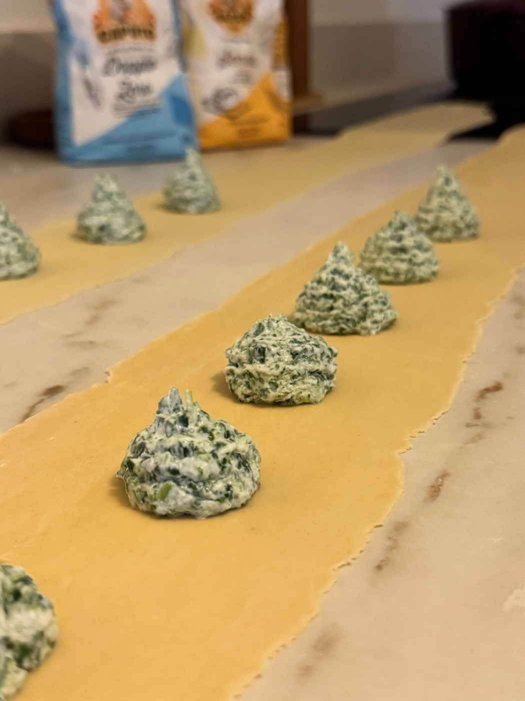 Een rij bolletjes ricotta-spinazievulling op uitgerold pastadeeg